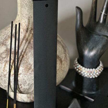 Minimalist black incense sticks beside a matte black holder, styled with a textured ceramic vase and a decorative hand sculpture wearing a beaded bracelet.