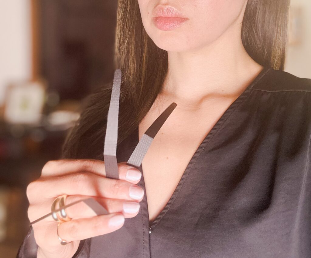 UX BOXES® Scent Spooling™ Perfume Scent Strips | A cropped portrait of a female in a room against a blurred background holding two black teardrop scent spooling perfume scent strips.