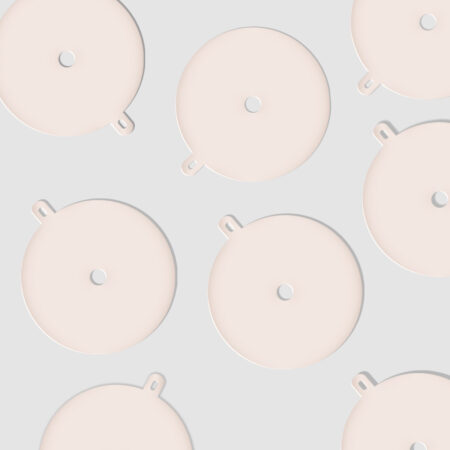 Flat lay of round cream-colored candle dust covers with small arched pull-tab die cuts, arranged in a repeating pattern on a soft gray background with subtle shadows.