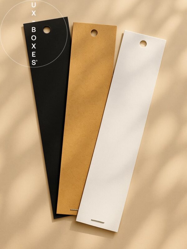 UX BOXES Trademark | Three sun-dappled overlapped envelopes with hang-holes laying flat on a light beige surface. A white envelope in the front of the overlapping a kraft and black envelope.