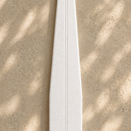 Tall matte white scent strip with elongated tapered silhouette and soft porous texture resting on a creamy sandstone surface with natural leaf-shadow lighting.