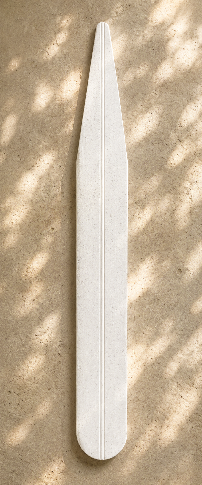 Long sculptural white fragrance strip with rounded base, subtle porous texture, and centered groove displayed on warm sandstone with filtered sunlight.