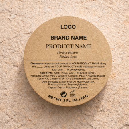 Circular kraft paper label mockup placed on a textured sandstone surface, featuring a natural warm brown tone with visible paper grain. The centered black typography includes “LOGO,” “BRAND NAME,” and “PRODUCT NAME” in a clean, minimal hierarchy, followed by smaller italic subtext for product features and scent. A thin horizontal divider separates the top from detailed directions and ingredient list below. At the bottom curve, small cosmetic symbols and “NET WT. 2 FL. OZ. | 28 G” are printed, all lit with soft, warm lighting that enhances the tactile, organic feel of the kraft material.