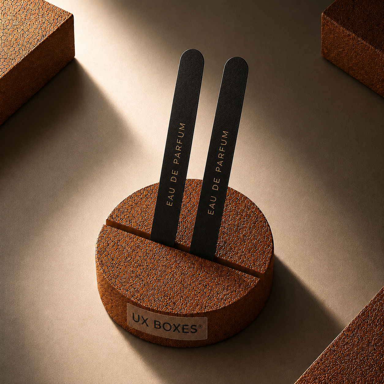 Luxury round cork perfume scent strip holder with dual black rounded-edge fragrance testing strips displayed vertically in a center groove, featuring a clear “UX BOXES®” front label under dramatic warm directional lighting.