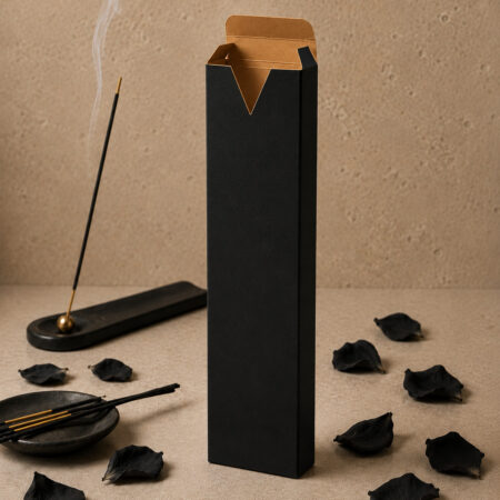 Luxury black incense tuck box with a kraft interior and signature V-cut opening, displayed open beside a burning incense holder and scattered black flower petals on a warm stone background, highlighting the premium contrast between the matte black exterior and natural kraft interior.