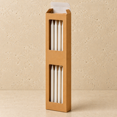 Tall kraft cardboard candle box with two rectangular display windows revealing four slim white taper candles. Open tuck-top packaging with white interior flaps shown in a clean studio setting against a beige stone-textured background.