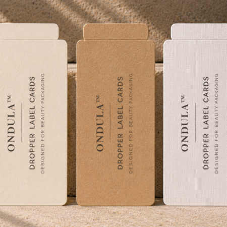 Three Ondula™ dropper label cards in cream, kraft, and white linen textured cardstock displayed against a natural stone background.