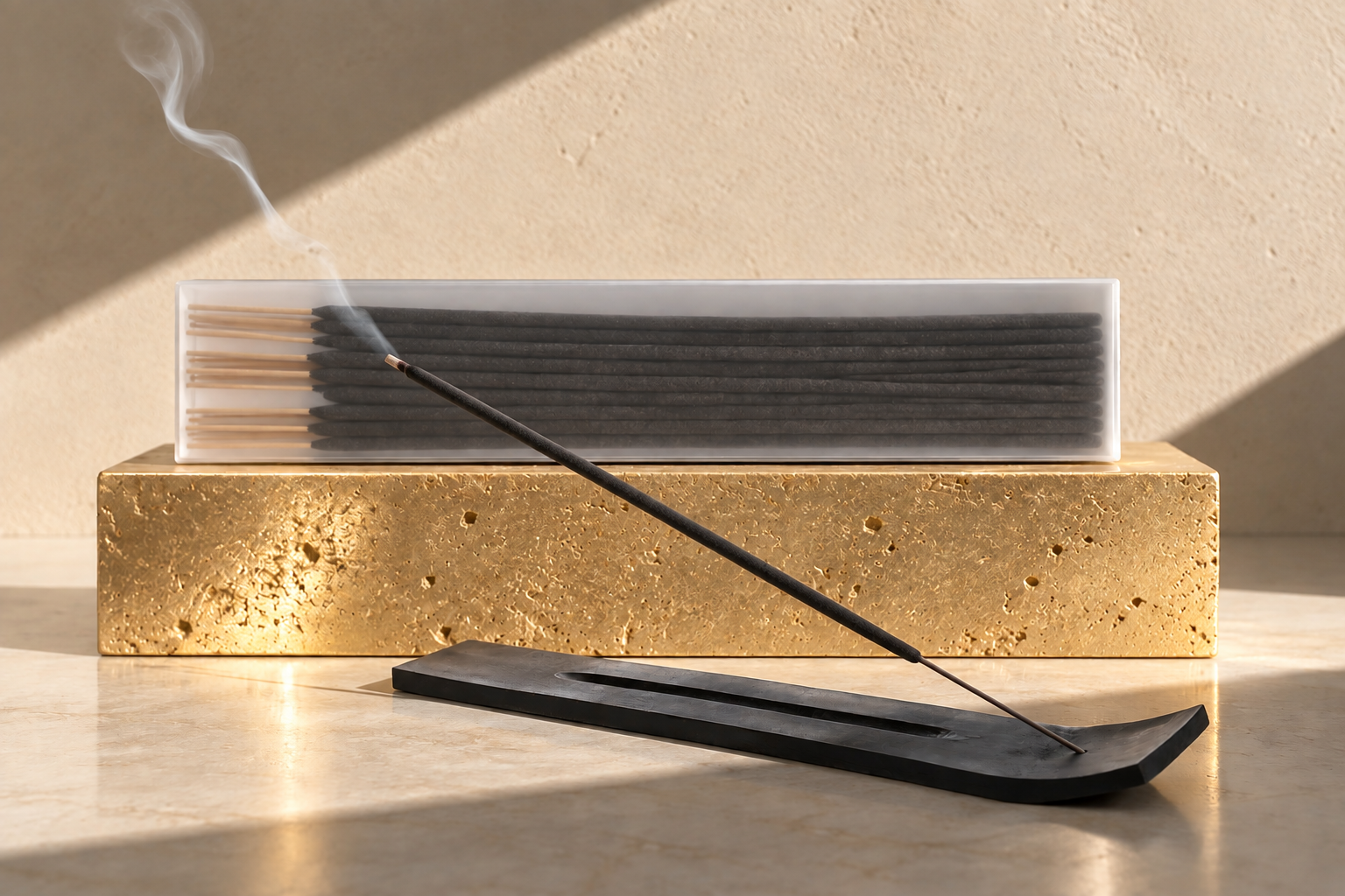 Black incense stick burning in a matte black holder beside packaged incense sticks displayed on a textured gold stone pedestal with stark directional lighting.