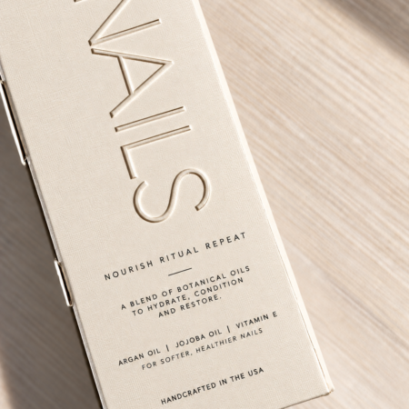 Creamy white linen-textured nail care box with embossed NAILS lettering, black printed details, and soft natural lighting.