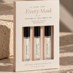 Cream textured perfume oil rollerball set with three glass fragrance vials, black caps, blush insert, minimalist typography, and soft natural lighting.