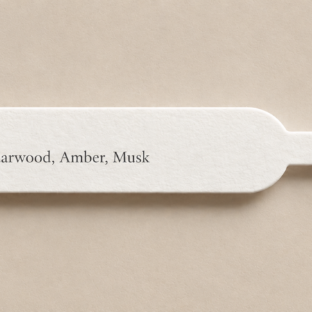 White perfume blotter strip printed with a scent profile in serif typography on a warm beige background.