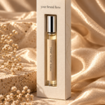 Luxury cream textured perfume box with a single glass rollerball bottle, silver cap, kraft label, and vertical display window, styled against shimmering champagne satin and natural stone.